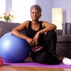 Senior Black woman sitting on floor with exercise equipment